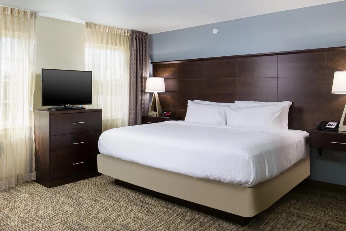 A warmly lit bedroom featuring a plush king-size bed, a wall-mounted flatscreen TV, and a functional nightstand. The room exudes a comfortable and restful atmosphere, perfect for relaxing after a long day. Soft linens and subtle decor add to the sense of tranquility.