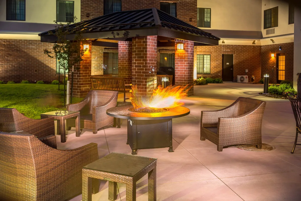 An exterior BBQ area featuring a brick structure, fire pit, and comfortable outdoor seating. The scene invites guests to relax and socialize in a cozy, alfresco setting, perfect for evening grilling or enjoying casual gatherings with friends and family.