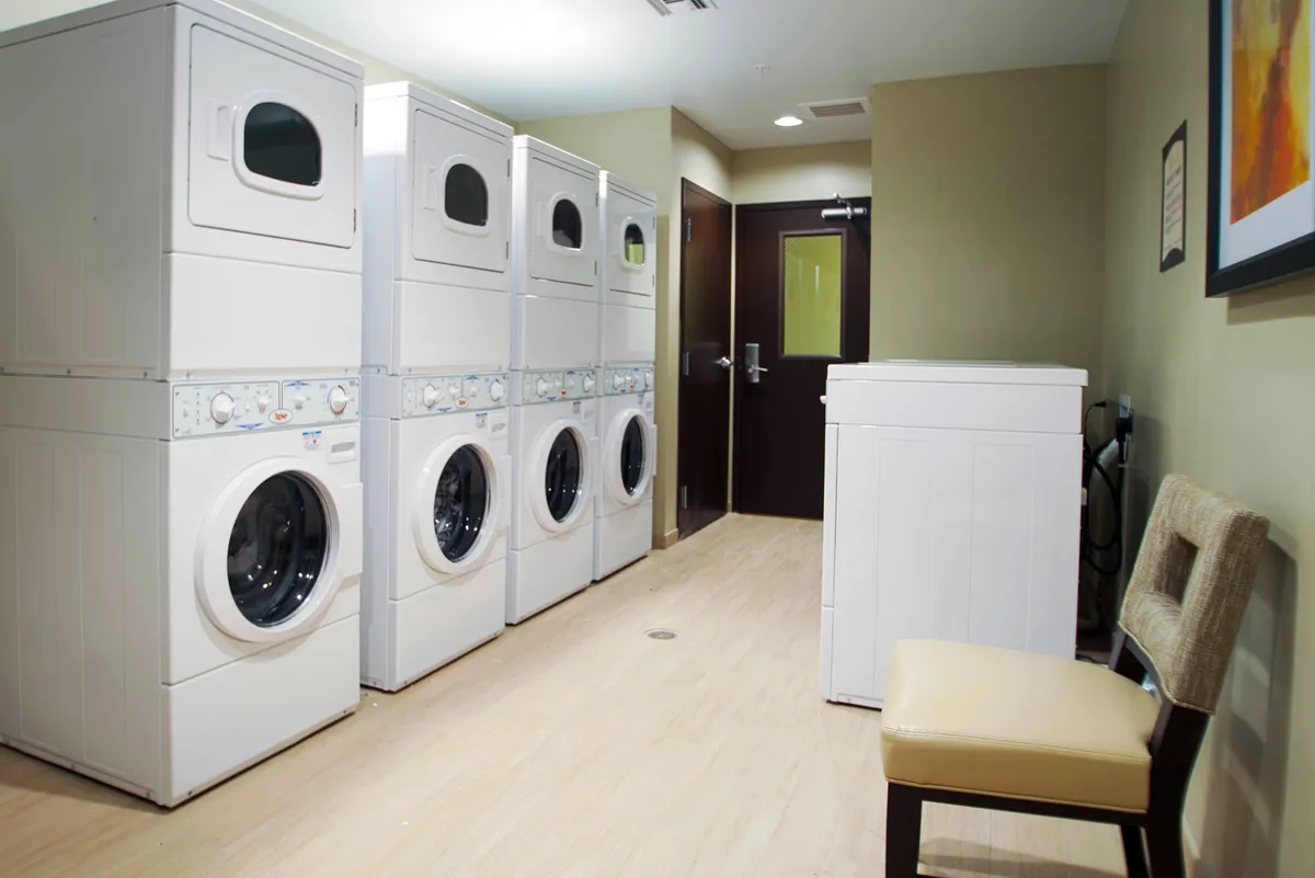 A well-lit laundry room featuring stacked washer-dryer units and a single washing machine, alongside a comfortable chair. The clean, practical space emphasizes convenience for longer stays and stress-free living.