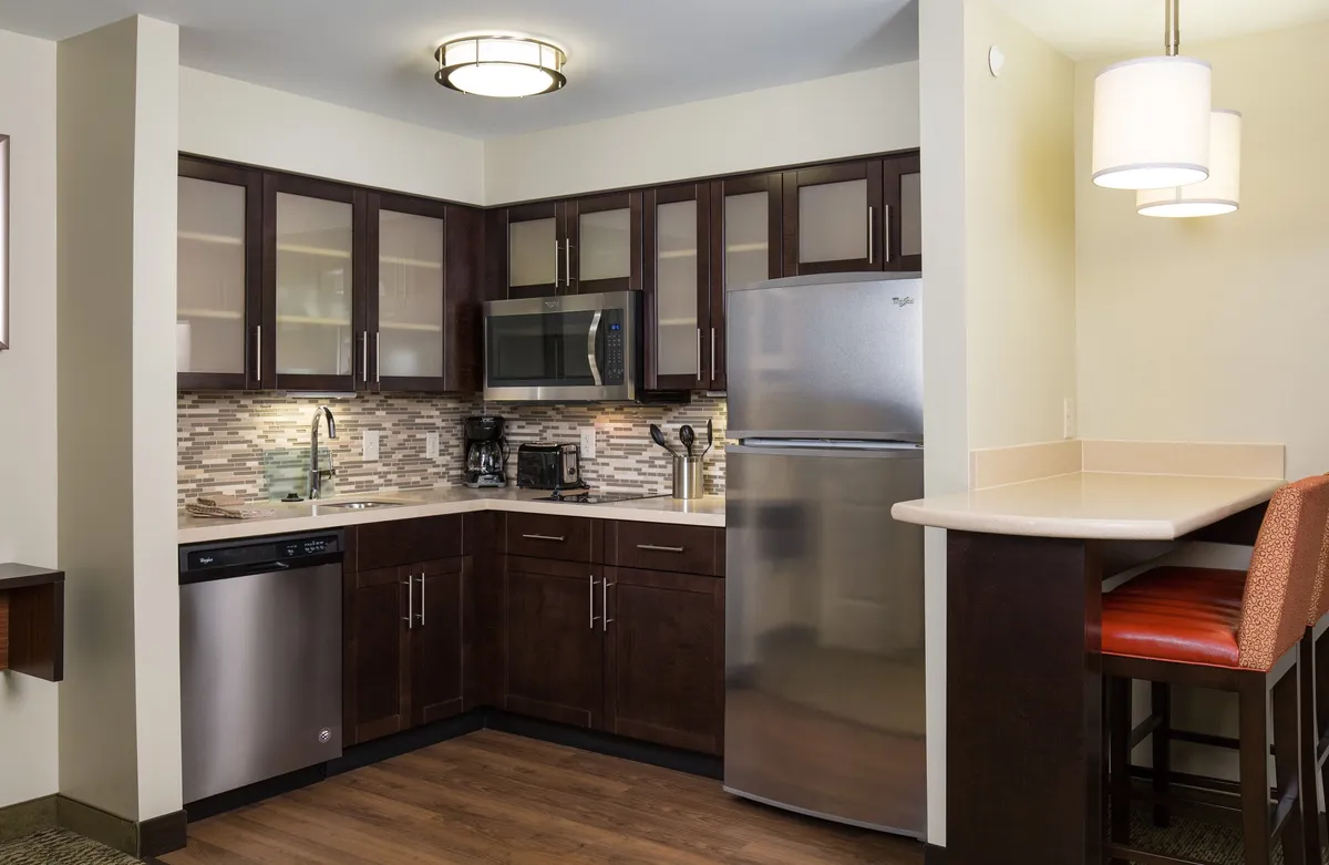 This image showcases a modern kitchen with stainless steel appliances, dark wood cabinetry, and stylish light fixtures. The space features countertop seating, creating a welcoming area for meal preparation, casual dining, and socializing. The kitchen is clearly equipped for cooking and entertaining, with appliances and utensils visible, reflecting a comfortable and functional atmosphere.